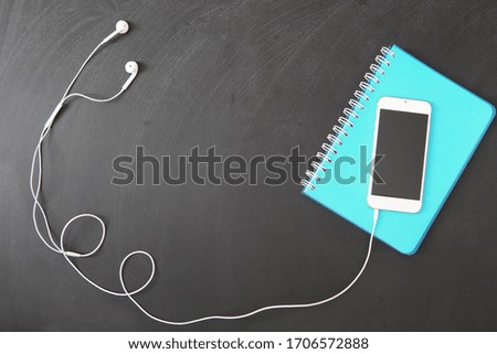 Remote learning background, smartphone with headphones and notebook on black chalkboard, online learning, distance education concept, space for text, top view.