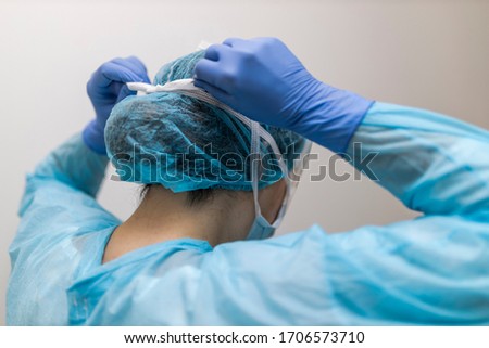 unrecognizable young nurse tying her respirator with protective clothing Royalty-Free Stock Photo #1706573710