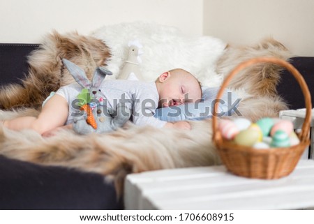 Little baby boy sleeping on a sofa on blue pillow and artificial fur, surrounded by easter decorations - bunny and basket with eggs