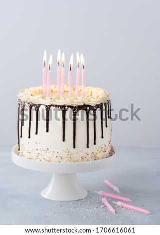 White birthday drip cake with sprinkles, chocolate icing and candles on a light blue background with copyspace. Trendy party decor cake concept.