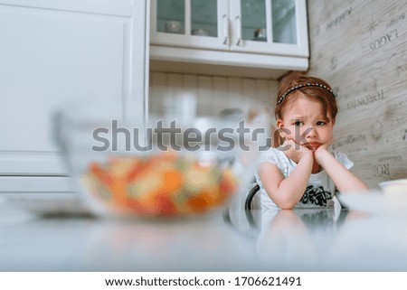 The girl in the kitchen is sitting at the table and is bored