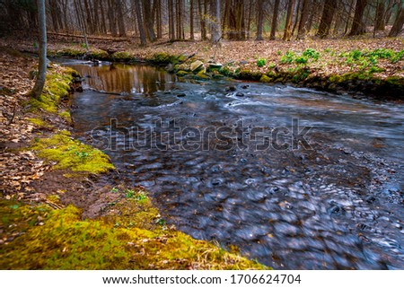 A slow shutter speed photograph of a stream flowing gently through the woods from a reflective pool