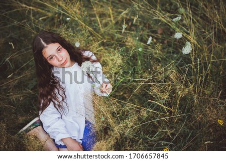 Small girl in blue dress sitting in the field of green grass 