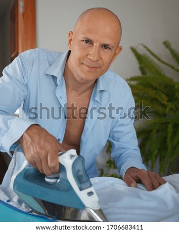 A single man is happy to iron his shirts.