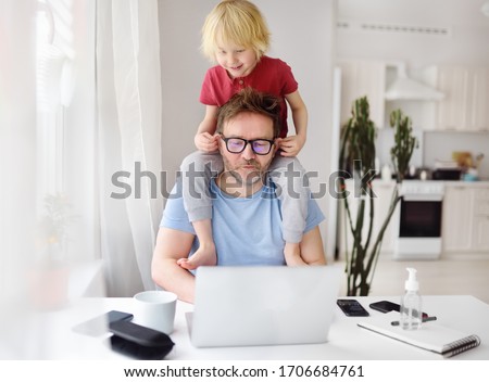 Man working from home with laptop during quarantine. Home office and parenthood at same time. Exhausted parent with hyperactive child. Chaos with kids during isolation
