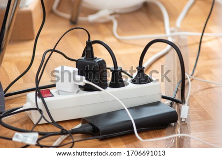 Messy outlet power extension cord on an apartment floor with various charging devices plugged in 2020 Royalty-Free Stock Photo #1706691013
