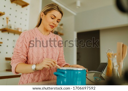 Close photo of young blonde woman in pink sweater preparing meal in kitchen at home. Young woman is cooking at home quarantine.