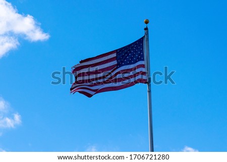 Tattered US Flag pulled taught in the wind against a blue sky with whispy clouds.