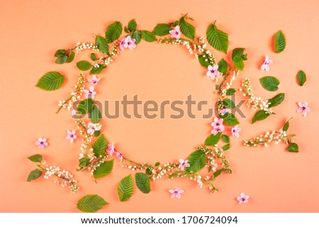 Round frame made of fresh spring texture leaves of different sizes with pink flowers on a bright background. The concept of spring flowering and renewal.