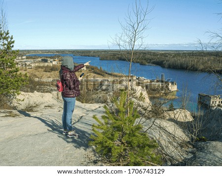 Hiker on mountain top with smartphone. Woman is standing and taking a picture on smartphone. Abandoned Quarry Of Rummu, Estonia. Scenic View Of Land Against Clear Blue Sky. Panoramic View. 