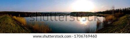 Beautiful spring sunset near lake with blue sky, green trees and water with reflection
