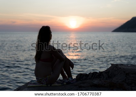 Silhouette of a young girl at the beaching watching the sunset Royalty-Free Stock Photo #1706770387