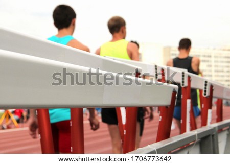 White and red fences at a sports stadium with athletes on a blurry background. Sports and healthy lifestyle