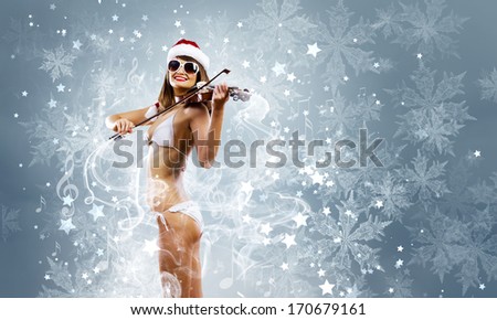 Young woman in swimming suit and santa hat playing violin