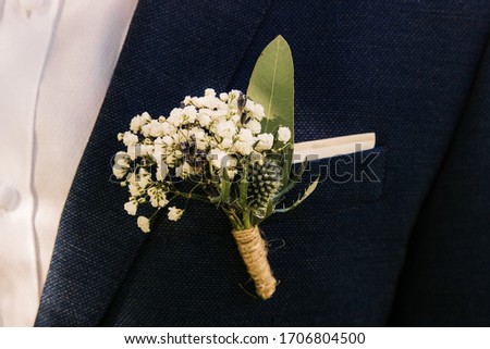 A detailed picture of the grooms flower pinned on a suit. Trendy small white cute flowers