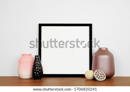 Mock up black square frame with vase home decor. Wooden shelf against a white wall. Copy space.