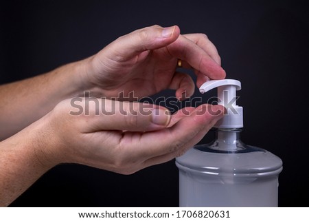 Hand receiving and hand operating the faucet of a disinfecting alcohol-based hand gel against a dark background. Studio shot of disinfection and health care situation. Royalty-Free Stock Photo #1706820631