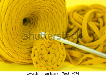 Knitting hook with a knitted fabric on a background of a ball of yellow yarn. Close-up