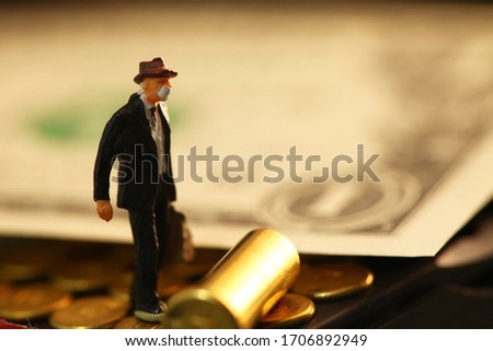Miniature male figure wearing mask among bullet shell and banknote background scene.