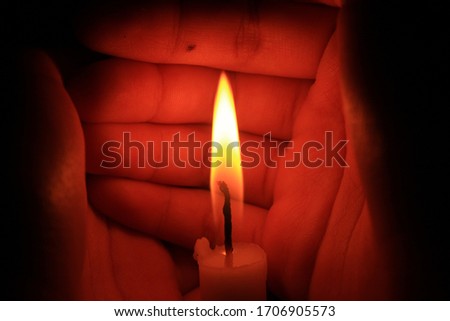 A pair of hands protect the candle flame in the darkness.
