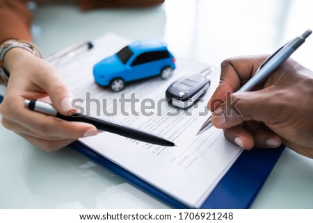 A Person's Hand Signing Car Loan Agreement Contract With Car Toy On Glass Desk
