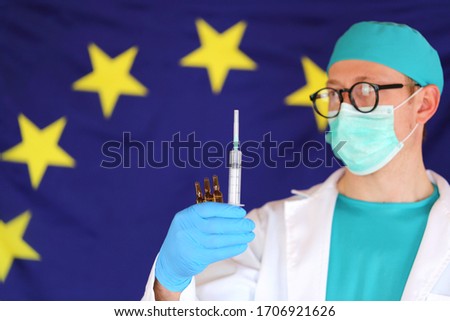 Virus vaccination in the European Union. Coronavirus infection  in Europe.Doctor in protective medical mask with a syringe in his hands on a European flag background.Prevention of the virus