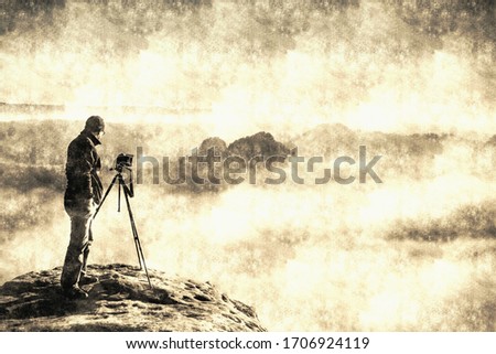 Landscape with a man in top of a peak taking photos with his camera on the stick at sunset.  Calotype filter. Old photo style.