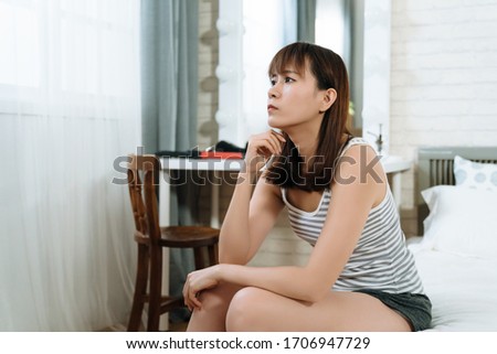 young asian lady getting up in morning is thinking about her plan for the day in her room. beautiful korean woman sitting and touching her chin is contemplating the meaning of life by the bedside. Royalty-Free Stock Photo #1706947729