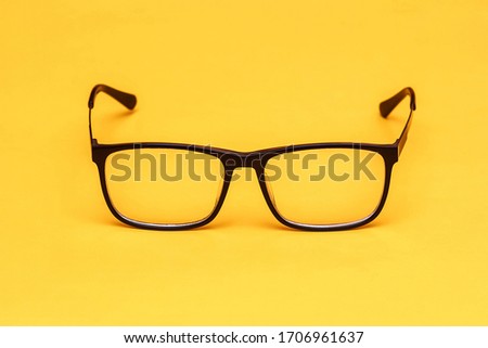Black eyeglasses with transparent lenses isolated on a yellow background. A stylish accessory. Design element. Top view. Close up. Copy space. 