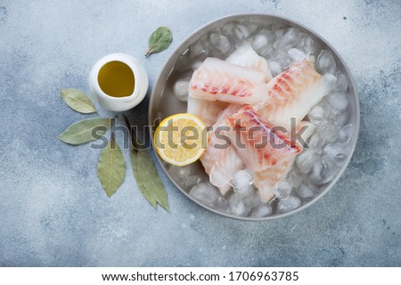 Fresh uncooked iced codfish fillet with seasonings over light-blue stone background, top view, horizontal shot