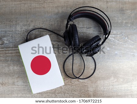 Headphones and book. The book has a cover in the form of Japan flag. Concept audiobooks. Learning languages.