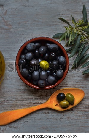 Bowl with black and green olives, near the olive branch and a wooden spoon
