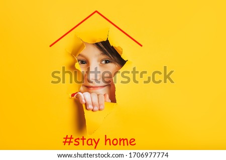 Funny child face looks in the hole. Kids on self-isolation at home during the COVID-19 coronavirus pandemic concept. House symbol on yellow background. Hashtags stayhome. Royalty-Free Stock Photo #1706977774