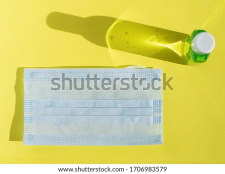 Sanitizer and face medical protective mask on yellow background. Flat lay, copy space, top view, shadow. Concept of disease, coronavirus, infection, hygiene