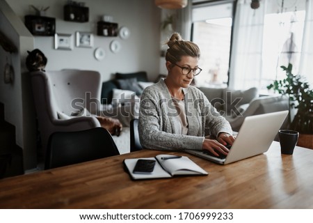 Businesswoman working on laptop computer sitting at home and managing her business via home office during Coronavirus or Covid-19 quarantine Royalty-Free Stock Photo #1706999233