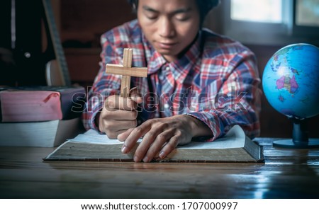 Asian man is holding the cross on Bible and pray. God's teachings according to belief and faith in God. Close up hand. Religion Concept.
