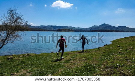 Two boys playing, immersed in the nature of a Sicilian lake, between a clear sky, majestic trees and hills
