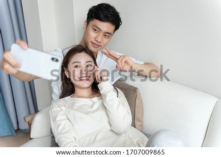 A young Asian couple taking pictures of each other on the sofa