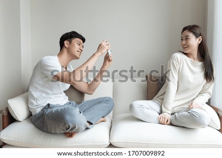 A young Asian couple taking pictures of each other on the sofa