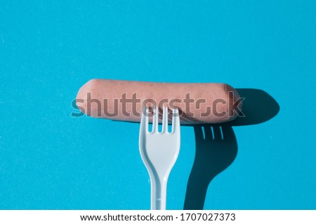 Raw sausage on a blue background with a plastic fork