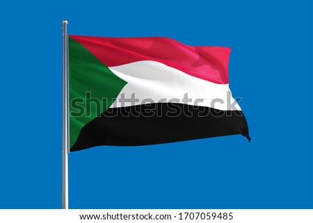Sudan national flag waving in the wind on a deep blue sky. High quality fabric. International relations concept. Royalty-Free Stock Photo #1707059485