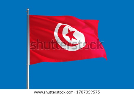 Tunisia national flag waving in the wind on a deep blue sky. High quality fabric. International relations concept.