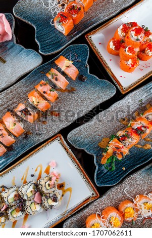 set of rolls on a black background in decorative plates: philadelphia, california, red caviar rolls, hot rolls vertical japanese menu top view 