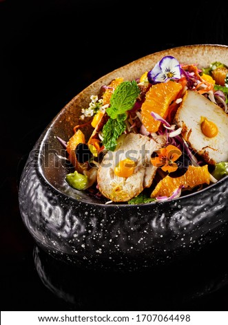 Mexican salad dish with sliced chicken mint leaves orange fresh pulps and flower decoration in black bowl. Food photography perfect for magazine or online delivery menu for restaurants.