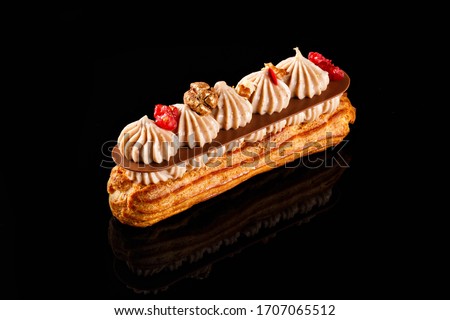 Eclair with cream filling and cranberry on top. Two layer of chocolate whip cream. Confectionary photography concept in black background.