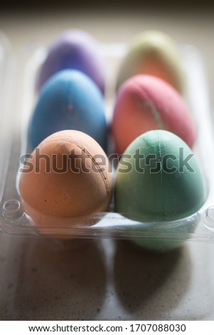 A half dozen carton of colorful chalk eater eggs lit by natural light from a nearby window seated on a stone table top

