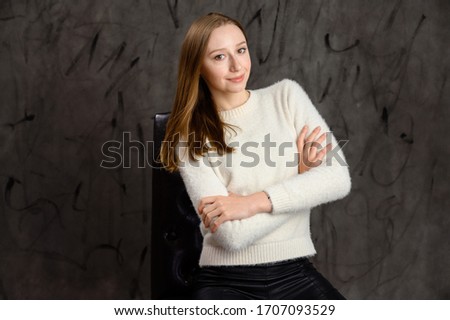 Studio portrait of a pretty happy blonde girl. Model posing on a chair on a gray stylish background.