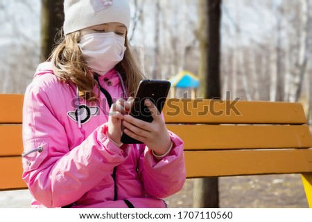 girl in medical mask with phone in her hands on the street in the park, protection from coronavirus, covid-19, SARS-CoV-2, qr code icon in the phone, omicron variant, lockdown, closeup