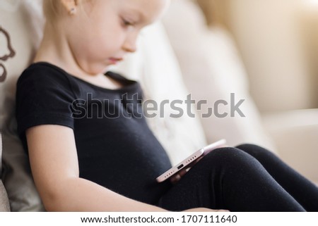 Distance learning, online education for kids. Happy girl holding smartphone in hands. Child watching online cartoons, kids computer addiction, parental control. Quarantine at home