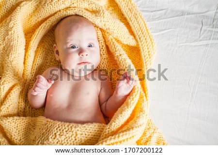 Cute infant baby looking at camera in a knitted yellow plaid on a white bed. Copyspace